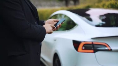 ROME, ITALY - 28 Nisan 2021: Roma 'da premium sınıfı araba kiralamak, yüksek kalifiye sürücü beyaz Tesla arabasının uzaktan kumandalı fonksiyonlarını gösteriyor, akıllı telefon uygulamalarını pille şarj eden adam