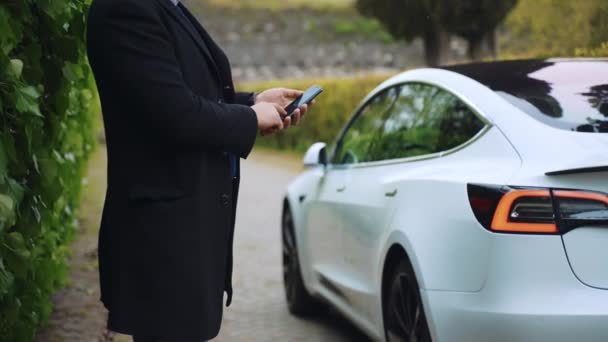 ROMA, ITALIA - 28 APRILE 2021: Elegante uomo che utilizza l'app per smartphone per il telecomando dell'auto Tesla bianca di classe premium, conducente che si avvicina a distanza all'auto e apre la porta, futuristica smart car con — Video Stock