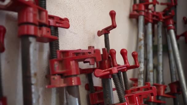 Tischlerei mit Arbeitswerkzeugen, Instrumenten und Geräten, Stahlklammern aus Holz, die an der Wand in der Werkstatt lehnen. Metallklammern und -klammern zum Anziehen von Holzstäben oder -planken nach dem Kleben — Stockvideo