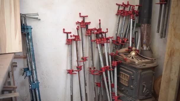 Esquina con herramientas pesadas de abrazaderas de madera en taller, abrazaderas y clips de diferentes tamaños utilizados para apretar tablones y barras de madera después de procesos de carpintería. Instrumentos y herramientas pesadas en carpintería — Vídeos de Stock