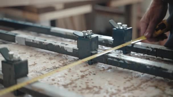 Close-up tiro de carpinteiros mãos segurando fita métrica e distância de medição entre três braçadeiras de aço na bancada, artesão usando régua para tomar medidas certas antes do processo de marcenaria — Vídeo de Stock