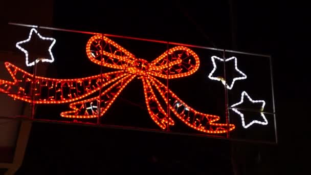 街路に吊るされ、道路を照らすクリスマスのきらびやかなLED装飾、さまざまな形と色冬の休日のお祝いの間に夕暮れに点滅するクリスマスライト。お祭り気分で — ストック動画