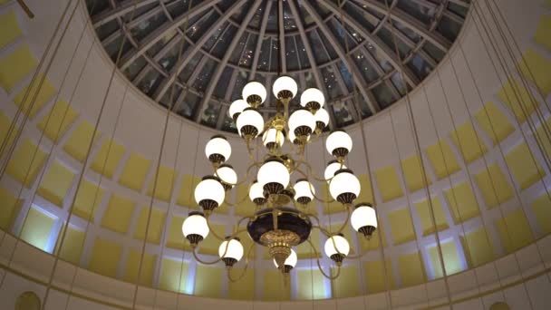 巨大的经典吊灯从圆形玻璃建筑穹顶伸展而下，带有人的动作倒影，简洁典雅的烛光照亮了建筑的内部。漂亮的老式吊灯 — 图库视频影像