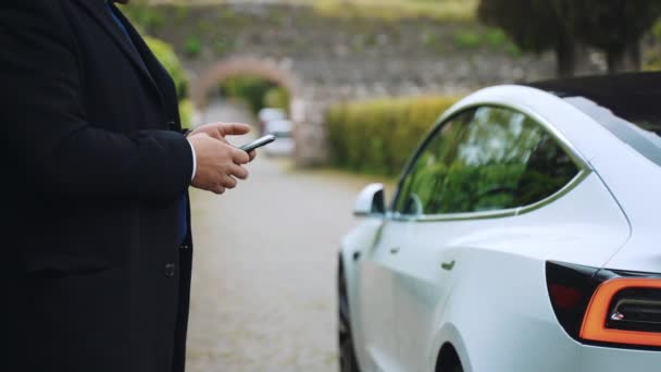 ROME, ITALIE - 28 AVRIL 2021 : Télécommande de véhicule électrique à l'aide d'applications pour smartphones, homme d'affaires debout près de la voiture Tesla avec téléphone portable dans les mains, fonctions de l'application homme défilement, allumer et éteindre — Video