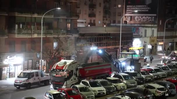 ΡΩΜΗ, ΙΤΑΛΙΑ - 9 ΑΠΡΙΛΙΟΥ 2021: Νυχτερινές εργασίες στο δρόμο της Ρώμης, ομαδικοί εργάτες αφαιρούν κατεστραμμένη άσφαλτο με αλεστική μηχανή λείανσης και ρίχνουν σκόνη ασφάλτου στο φορτηγό. Εργασίες επισκευής σε — Αρχείο Βίντεο