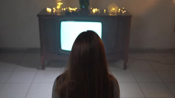 Câmera zoom na mulher sentada na frente da televisão vintage com cintilação quebrada e tela listrada, visão traseira da mulher morena se sentindo sozinha em casa em isolamento. Tela de TV retro, passando tempo — Vídeo de Stock