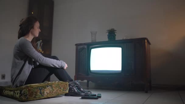 Samotna kobieta w izolatce oglądająca telewizję w domu, smutna kobieta siedząca na poduszce na podłodze i oglądająca stary telewizor retro z pstrykającym ekranem. Nudny nastrój atmosferyczny w pokoju o zmierzchu z zabytkowymi meblami — Wideo stockowe