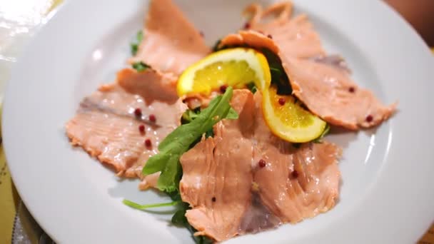 Rodajas sazonadas de pescado de salmón rojo de lujo en plato blanco, manjar mariscos mediterráneos en el restaurante. Rebanadas de salmón ahumado con pimienta, ensalada de rúcula y rodajas de limón. Restaurante mediterráneo — Vídeo de stock