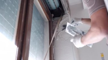 Profesyonel inşaat işçisi merdivenin üzerinde duruyor ve duvarları eski dış paten panjurlarıyla kirli pencerenin yakınına beyaz macun solüsyonuyla kaplıyor. Koruyucu yapıcı