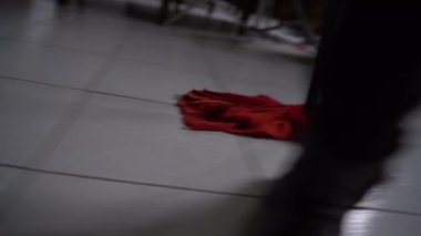Siyah çizmeli hademe dairede ya da ofis odasında yer arıyor, temizlikçi kirli zemini temizlemek için ıslak kırmızı paspas kullanıyor. Temizlik zemini dezenfektan deterjan ve paspasla temizleniyor.