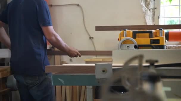Συμπυκνωμένος τεχνίτης σε εργαστήρι λείανσης ακατέργαστων ξύλινων ράβδων με ηλεκτρική μηχανή λείανσης, επαγγελματίας ξυλουργός που εργάζεται με διάφορα είδη δέντρων κατασκευάζοντας έπιπλα υψηλής ποιότητας στο χώρο εργασίας — Αρχείο Βίντεο