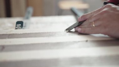 Marangoz, ahşap tahta yüzeyden endüstriyel bıçakla tutkal kalıntıları temizliyor, atölyede ahşapla çalışan bir zanaatkar, iki ağaç çeşidiyle ahşap ahşap ahşap ahşap kaplama yapıyor, demir çubuklarla bağ kuruyor.