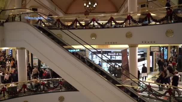 ŘÍM, ITÁLIE - 19. prosince 2019: Slavnostní nálada ve slavném římském nákupním centru s červenými vánočními ozdobami, podlahami a eskalátory zdobenými větvemi stromů, červenými míčky a stuhami. Lidé utrácejí — Stock video