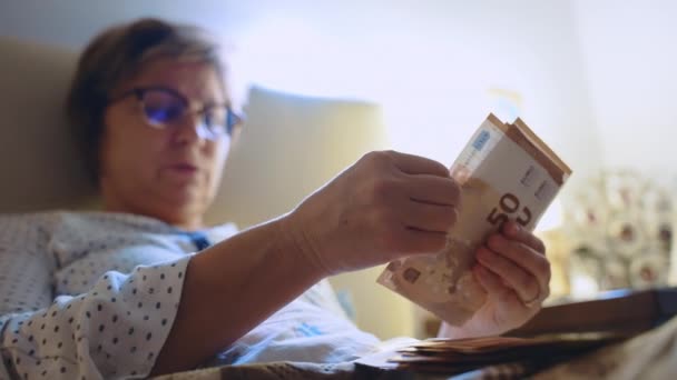 Socio financiero de mediana edad acostado en la cama y contando dinero sucio, mujer con anteojos calculando el dinero de la corrupción en casa. Transacciones financieras ilegales en el ámbito bancario y comercial, dinero — Vídeo de stock