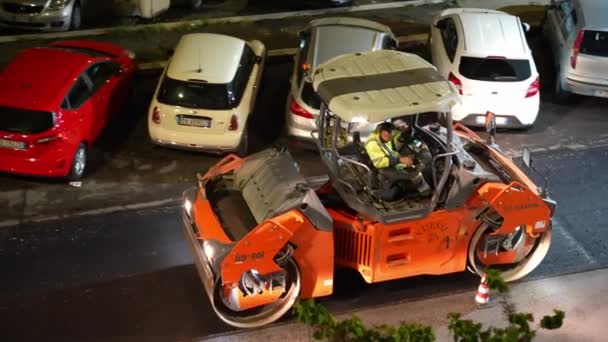 로메 , ITALY - APRIL 9, 2021 년 4 월 9 일: 오렌지 산업 롤러코스터를 운행하는 제복을 입은 운전자, 길을 따라 증기가 올라오는 신선 한 아스팔트를 평준화하고, 밤에 도로 위에서 재건 작업을 하는 모습 — 비디오