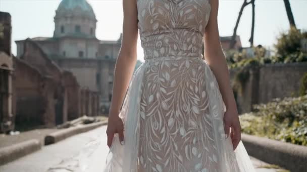 Modelul tânăr la modă în rochie elegantă de mireasă din dantelă mergând încet pe Forumul Roman și pozând pe cameră, performanța anuală a îmbrăcămintei de mireasă la modă, frumusețea și conceptul de modă — Videoclip de stoc