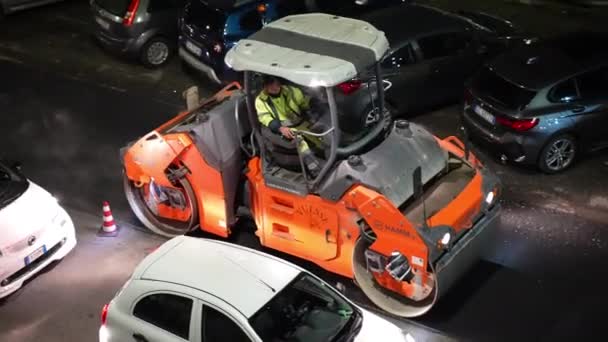 ROME, ITALIE - 9 AVRIL 2021 : Travailleur en uniforme conduisant une machine à paver industrielle nivelant de l'asphalte chaud frais et fumant le long de la rue, travaux de reconstruction sur la route la nuit, route goudronnée — Video