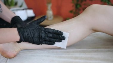 Güzellik salonunda cilt bakımı ve tüy dökme prosedürleri, siyah eldivenli kozmetoloji uzmanı kadın bacaklarında büyüyen kılları çıkarıyor ilk önce ısıtmalı tüy dökücü ağda uyguluyor ve sonra tüy dökücü ile yırtılıyor.