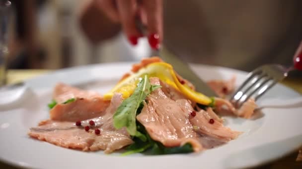 Catering service van luxe mediterrane restaurant, mode vrouw snijden sappige rode zalm plakjes met vork en mes, delicatesse plaat gekruid met citroenschijfjes, peper, olijfolie en raket salade — Stockvideo