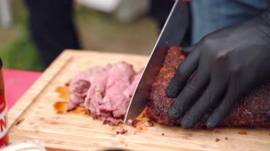 Barbekü şefi az pişmiş sığır filetosunu çıtır çıtır ile ince ince dilimliyor, profesyonel pişirme bıçağını geleneksel barbekü pikniğinde et dilimlemek için kullanan adam. Sulu baharatlı.