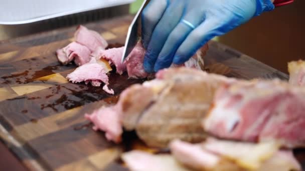 BBQ experiences in gloves slicing thinly medium rare grilled meat tenderloin with professional cooking knife on wooden board, chef slicing meat fillet for guests of picnic party. Grilled meat slicing — Stock Video