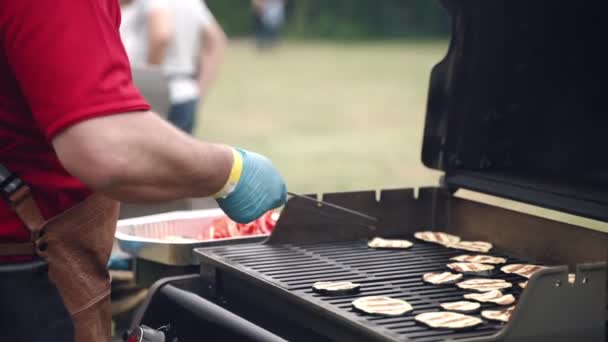Eldivenli ve önlüklü bir adam, ızgara patlıcan dilimlerini bbq ızgarasından çıkarmak için yemek maşası kullanıyor, şef yemek servisi için mangal kömüründe sebze kızartıyor. Geleneksel barbekü festivali — Stok video