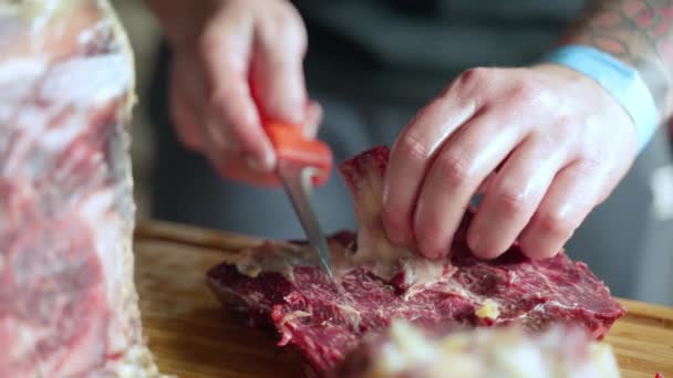 Carniceiro profissional cortando costelas de porco cruas frescas no matadouro e se preparando para a venda, o homem separa a gordura da carne com faca de cozinha na placa de cozimento g. Processo de fabricação de carne, alimentos — Vídeo de Stock