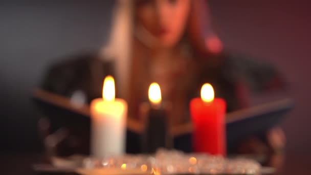 Bougies blanches, noires et rouges brûlant sur fond de sorcière dangereuse lisant un livre noir et une potion d'orthographe, de sorcellerie effrayante et de rituels paranormaux avec vie après la mort — Video