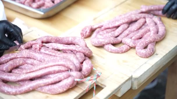 Preparation for BBQ picnic party, chef in black gloves preparing long fresh meat sausages for roasting on hot charcoal in smoker or barbecue grid. Bratwurst sausages for barbecue grilling, bbq picnic — Stock Video