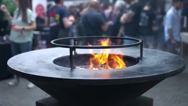 Increíble incendio en el interior de la barbacoa redonda negro fumador, personas borrosas en el fondo preparándose para el festival de barbacoa tradicional. Quema de carbón para asar y asar alimentos en la fiesta de picnic — Vídeos de Stock