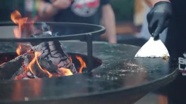 Professional barbecue man in black gloves using metal spatula for cleaning burnt surface of black round bbq grid and cleansing food remnants. Process of cleaning bbq grid after roasting meat — Stock Video
