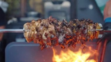 Dönen tükürüğün üzerinde kızgın domuz eti parçaları kızartılıyor, metal şişte yağlı et kızartılıyor. Eldivenli biri, BBC 'de sıcak kömür yakmak için metal maşa kullanıyor. Et kızartma.