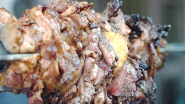 Primo piano colpo di grasso succosa carne di maiale fette arrosto su spiedo con pezzi di ananas tagliati, spiedo barbecue rotante sul fuoco ardente e grigliate sul fumo in aumento. Carne di maiale grassa con olio che cade, carne succosa — Video Stock