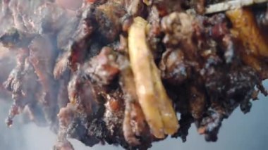 Dipteki görüntüde yağlı domuz dilimleri döner tükürük üzerinde kavruluyor ve kömürlerin üzerine erimiş yağ döküyor, kızgın ızgarada sulu yanmış domuz eti ve yükselen duman. Barbeküde kızarmış domuz eti.