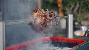 Hafta sonu piknik partisinde metal şiş giyen profesyonel barbekü içicisi, tükürük üzerinde dönen yağlı domuz ve dumanı tüten kömürde kavrulan. Barbekü festivali partisi. Kızarmış, sulu domuz eti.