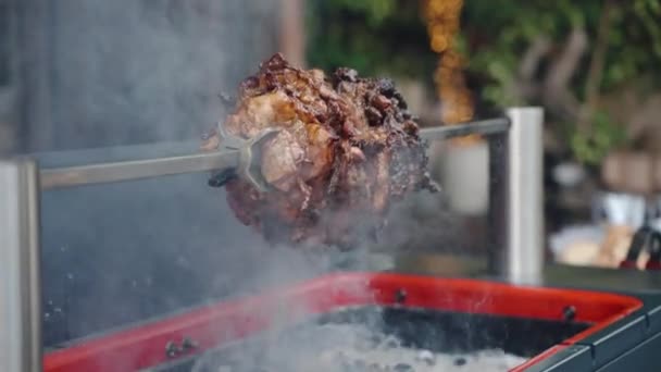 Professional barbecue smoker with metal skewer on weekend picnic party, fat juicy pork rotating on spit and roasting on smoking charcoals. Barbecue festival party with bbq roasting, juicy pork meat on — Stock Video