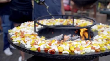Geleneksel barbekü pikniği partisi hafta sonu, şef kızarmış sebzeleri BBC ızgarasında pişirirken profesyonel zeytinyağı döküyor. Taze soğan, domates ve dolmalık biber ateşte kızarıyor.