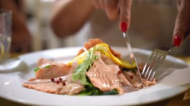 Akdeniz restoranında beyaz tabakta lezzetli kırmızı somon dilimleri tatmakta olan kadın ziyaretçi, biber, taze yeşil salata ve limon dilimli deniz ürünleri şarküterisi. Lüks pahalı tabak.