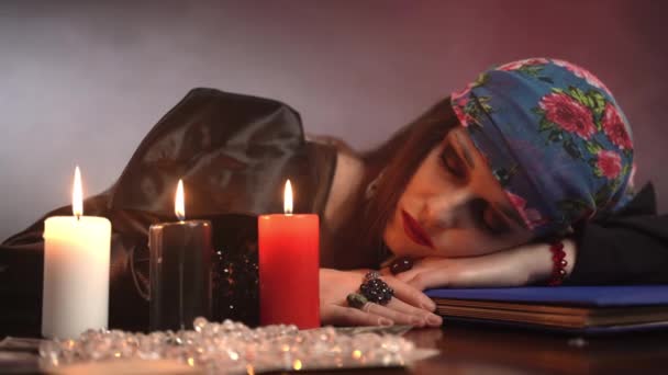 Satanische heks die aan tafel slaapt met drie brandende kaarsen en ritueel gereedschap, occulte zigeuners die mysterieuze rituelen uitvoeren, waarzeggerconcept — Stockvideo