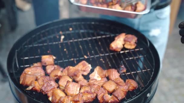 Tradycyjny piknik grillowy na świeżym powietrzu, ludzie pieką różne mięso na grillu siatki profesjonalnego palacza. Człowiek umieszczenie pieczone kawałki wieprzowiny w opakowaniu foliowym do jedzenia z członkami rodziny — Wideo stockowe