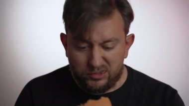 Beyaz arka planda hamburger yiyen aç bir adam komik yüz ifadelerini ve yüz ifadelerini gösteren bir erkek hamburgeri ısırıyor. Genç adam sağlıklı öğle ve akşam yemekleri yerine modaya uygun fast food yiyor.