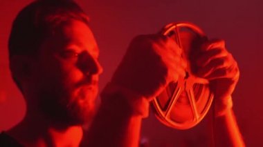 Sinematografi stüdyosunda çalışan profesyonel kameraman kırmızı ışıkla aydınlatılmış retro film makaralarını kuruyor, operatör retro bobinlerle çalışıyor projektöre takıyor ve kaydediyor veya izliyor.