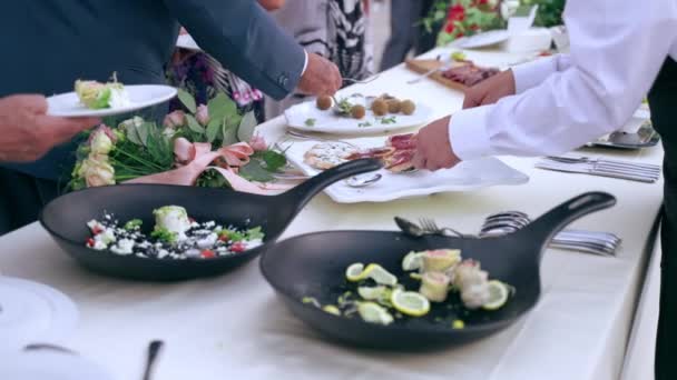 Oficjalne wyjście biznesmenów w luksusowej restauracji na świeżym powietrzu, kelner w mundurze obsługujący gości przy stole bankietowym oferujący wybór smacznych przekąsek i przekąsek na białych talerzach. Luksusowe — Wideo stockowe