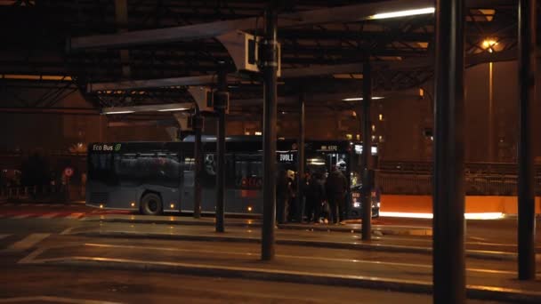 ROMA, ITALIA - 23 DE NOVIEMBRE DE 2020: Estación de autobuses pública en Roma por la noche, pasajeros subiendo al autobús en la plataforma. Cercanías públicas con inscripción de neón en el parabrisas — Vídeos de Stock