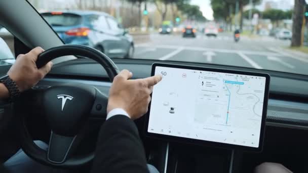ROME, ITALY - APRIL 28, 2021: Man driving autonomous Tesla car along the streets of Rome, changing function of LCD touchscreen monitor and driving with no-hands. Smart operating system of Tesla car — Stock Video