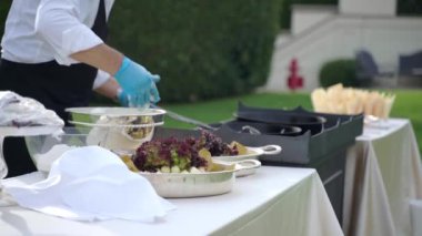 Özel Villa malikanesinin zarif bahçesindeki servis masasının yan görüntüsü, şef ziyafet masası için çeşitli atıştırmalıklar ve aperatifler hazırlıyor. Üniformalı garson meyve kesiyor.