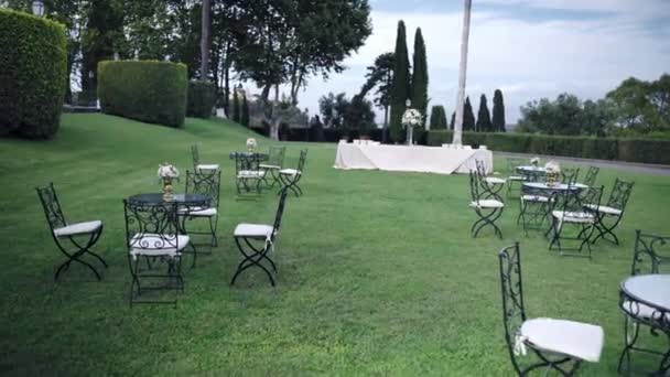 Réception extérieure magnifiquement décorée pour une cérémonie de sortie spéciale sur la cour avant de l'ancienne résidence privée, tables rondes noires et chaises agencées avec des bouquets de fleurs de mode. Invités formel — Video