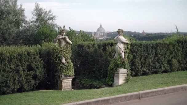 Dwa starożytne posągi o charakterze mitycznym porośnięte zielenią na tle majestatycznej kopuły watykalnej, zabytki zdobiące podwórko ekskluzywnej prywatnej willi włoskiej z niesamowitym — Wideo stockowe
