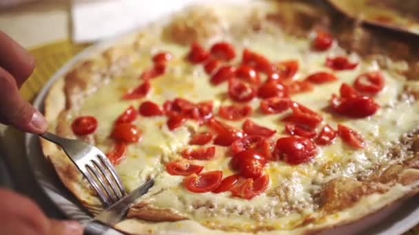 Верхній вид знімків з використанням столової виделки і ножа для різання смачної соковитої піци Маргарита в місцевій піцерії, чоловік розрізає гарячу печену томатну піцу на білій тарілці. Традиційний італійський раунд — стокове відео