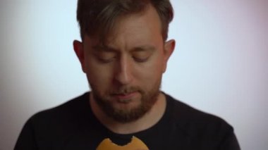 Aç bir adamın portresi fast food burgerini zevkle ısırıyor, tadıyor ve kafa sallıyor. Tatmin olmuş erkek elinde et pirzolası, sağlıklı yetişkinler sağlıksız yiyecekler, abur cubur yiyor.